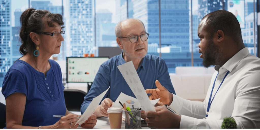Business consultant discussing financial documents with an older couple in an office, reviewing reports and planning next steps.