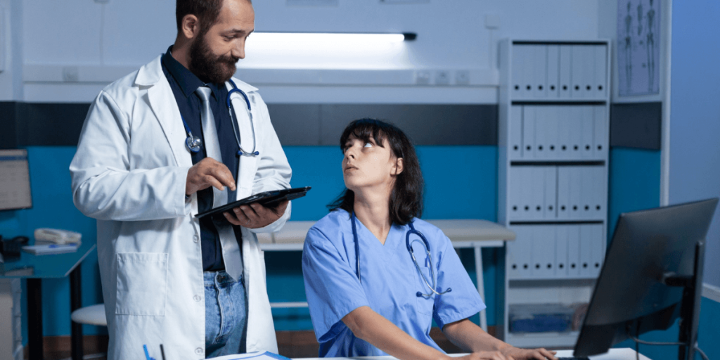 Doctor reviewing information on a tablet with a nurse in a clinic, discussing patient data and treatment details.